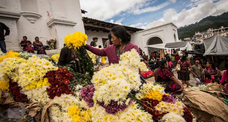 Indigene Blumenverkäufer arrangieren leuchtende Chrysanthemen außerhalb einer weißen Kolonialkirche während des Markttages.