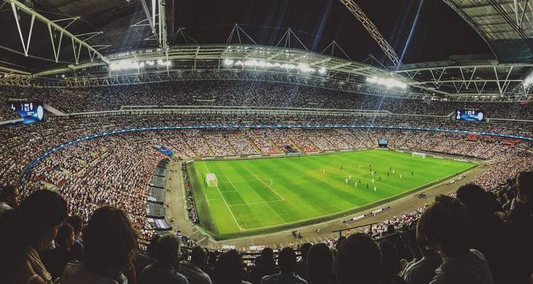Panoramisch nachtaanzicht van een volpakt voetbalstadion met felle schijnwerpers en groen speelveld
