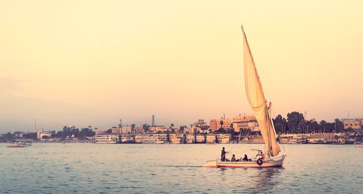 Une felouque traditionnelle à voile crème glisse le long du Nil dans la douce lumière du soir