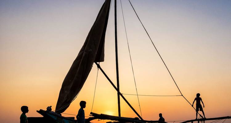 Traditionele zeilboot met kinderen in silhouet tijdens een gouden Sri Lankaanse zonsondergang op het water.