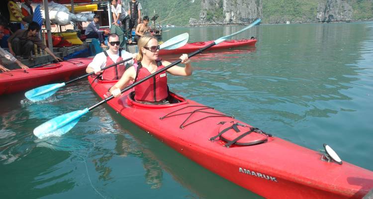 Touristen, die in roten Kajaks auf den türkisfarbenen Gewässern der Ha-Long-Bucht gegen Kalksteinklippen paddeln.