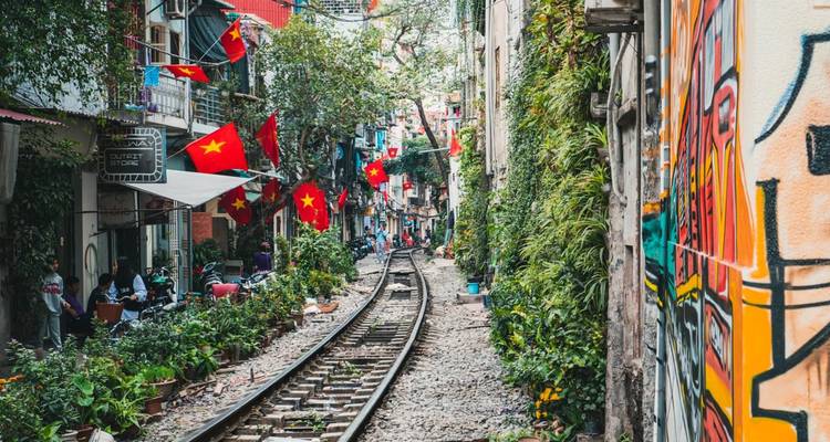 Enge Hanoi-Zugstraße mit Cafés und roten vietnamesischen Flaggen entlang der Eisenbahnstrecke.