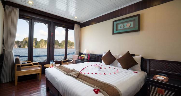 Elegante cruiseschipshut met kingsize bed, rozenblaadjes en groot raam met uitzicht op de kalksteenrotsen van de Baai van Halong.