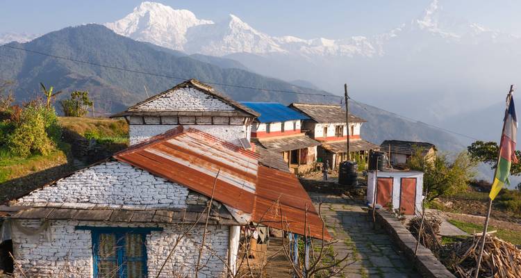 Stenen boerderijen met roestbruine daken met uitzicht op de mistige Himalaya-toppen