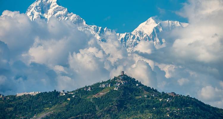 Met wolken bedekte Himalaya-toppen die hoog boven een groene heuvel met huizen uitsteken