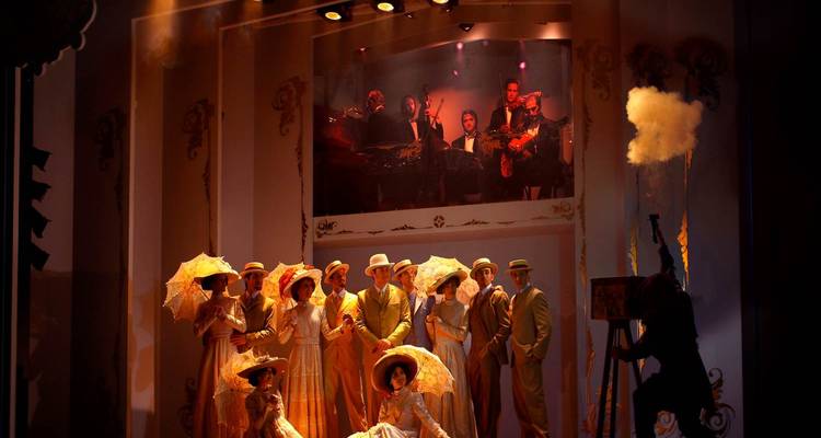 Kostümierte Darsteller, die auf einer Theaterbühne unter dramatischer Beleuchtung und Bühnenbild auftreten.