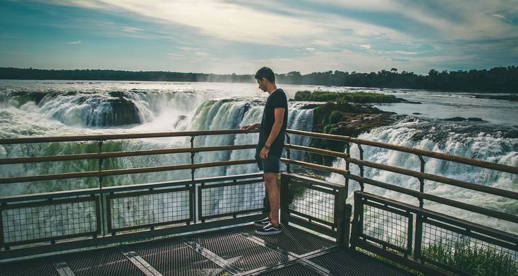 Junger Mann, der auf einer Aussichtsplattform steht und auf die riesigen Iguazu-Wasserfälle blickt.