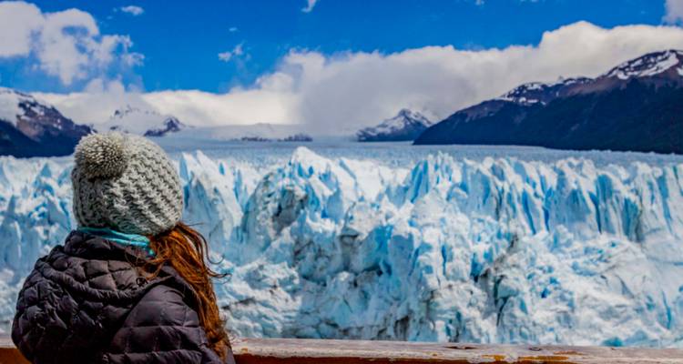 Ein Reisender in Winterkleidung blickt auf die aufragende blaue Eismauer des Perito-Moreno-Gletschers unter strahlend blauem Himmel.