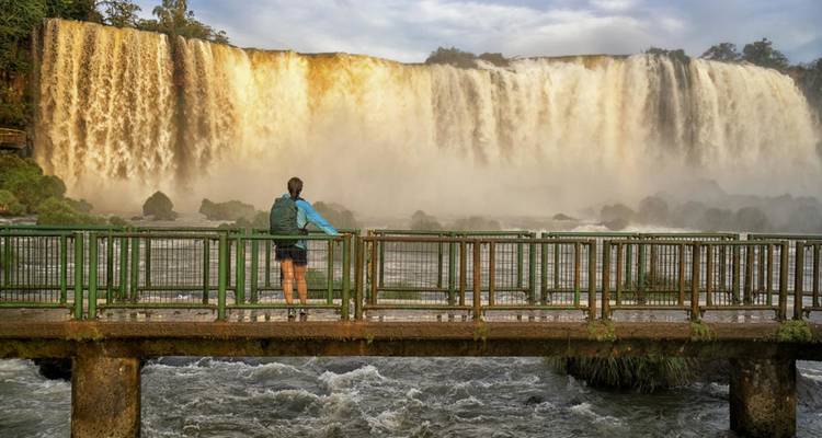 Ein Besucher auf einer Aussichtsplattform beobachtet die mächtigen Iguazu-Wasserfälle, die durch goldenen Nebel herabstürzen.