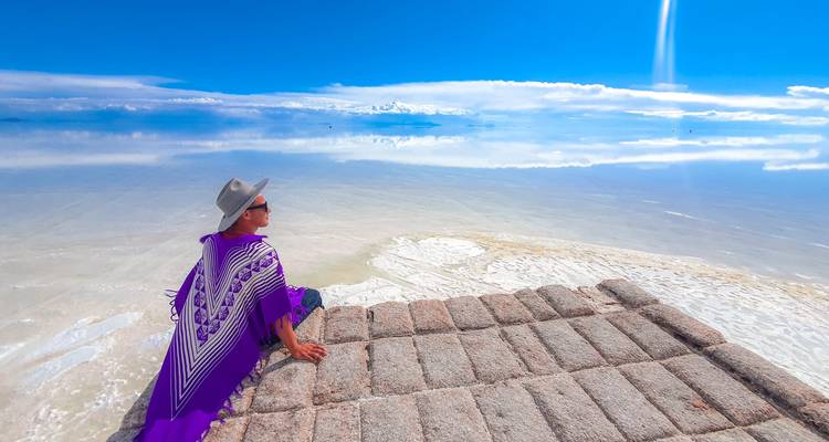 Reiziger in paarse poncho ontspannend op zoutsteenplatform met uitzicht op spiegelvlakke zoutpannen