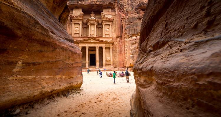 Bezoekers komen uit een smalle zandstenen gang tevoorschijn en zien de prachtige gevel van het Schatkistgebouw in Petra, omlijst door imposante rode rotswanden.