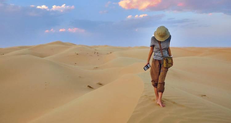 Un voyageur solitaire se promène pieds nus à travers les dunes dorées ondulantes sous des nuages de coucher de soleil aux teintes pastel dans les sables de Wahiba.