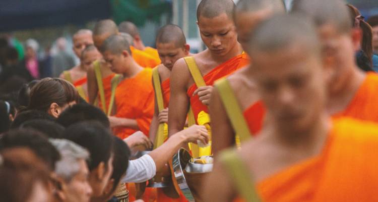 Rij met saffraan gekleurde monniken die tijdens de dageraadceremonie in Luang Prabang aalmoezen ontvangen van locals.