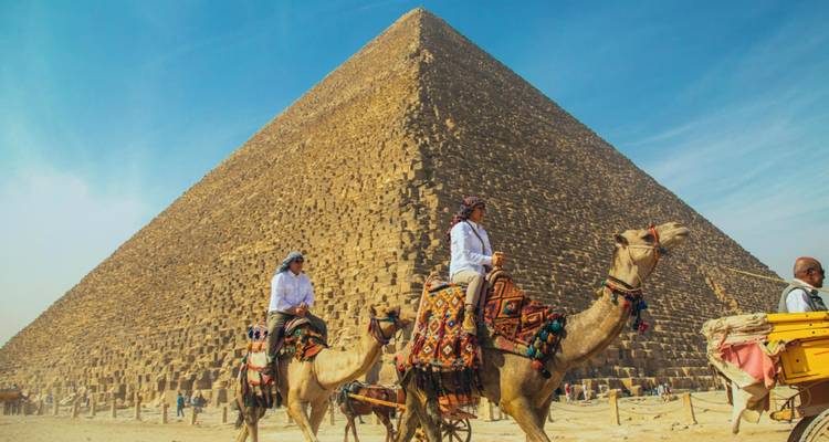 Des cavaliers sur des chameaux passent devant la Grande Pyramide de Giza sous un ciel bleu dégagé.