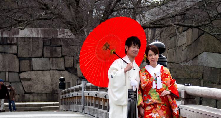 Stel in traditionele kimono's poseert onder een felrode paraplu op een houten brug.