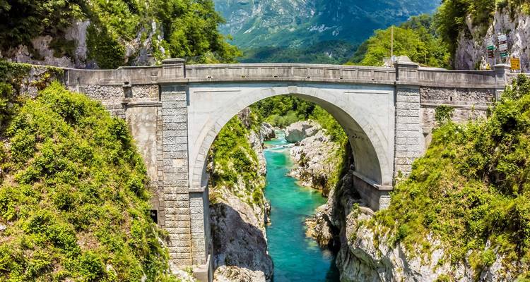 Pont en arc de pierre historique enjambant la rivière Soča turquoise entre des falaises de calcaire imposantes.