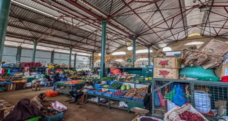 Bustling indoor produce market with colourful fruit stalls under a high metal roof.