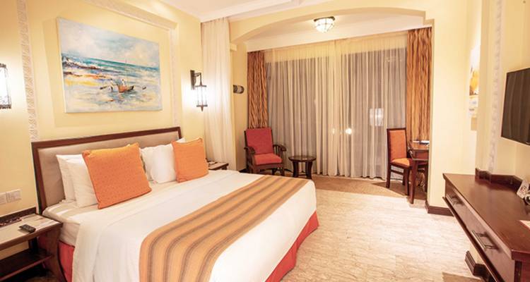 Warmly lit hotel bedroom with king bed, coral accents and seaside artwork.