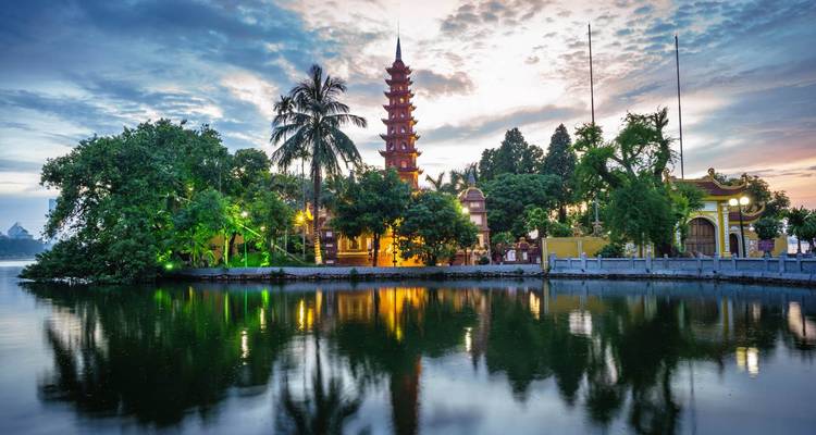 Die Tran-Quoc-Pagode und Palmen spiegeln sich in der ruhigen Oberfläche des Westsees bei Sonnenaufgang in Hanoi.
