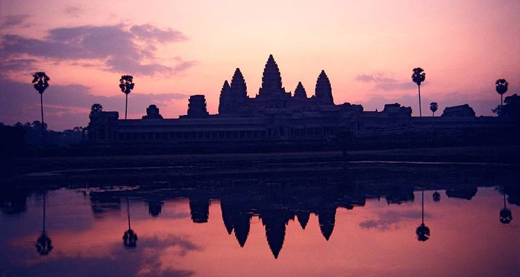 Silhouetten von Türmen von Angkor Wat spiegeln sich in einem ruhigen Teich vor einem magentafarbenen Morgenrot.