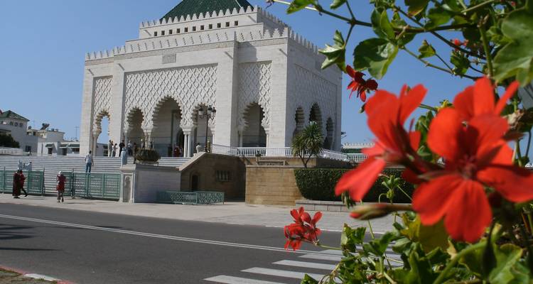 Mausoleo de mármol blanco con arcos ornamentados enmarcados por flores rojas en primer plano
