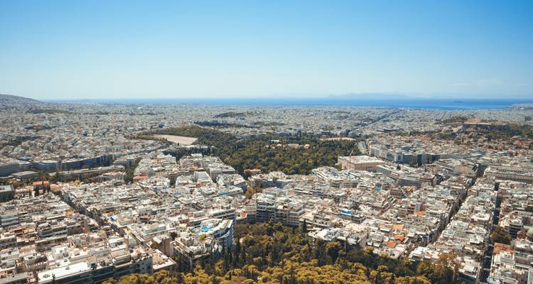 Vue aérienne panoramique de la vaste Athènes avec des parcs verdoyants au centre et la mer Égée à l'horizon.