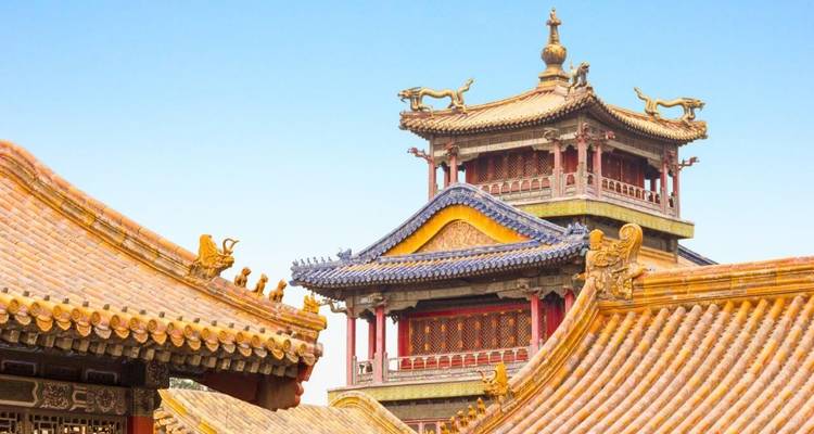 Sierlijke geel betegelde daken en decoratieve draken van een keizerlijk Chinees paleizencomplex tegen een heldere blauwe lucht.