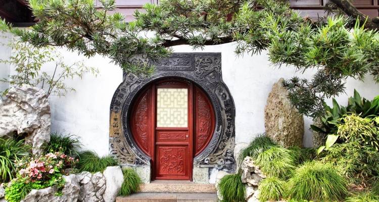 Uitgesneden cirkelvormige maanpoort die een rood houten deur in elkaar zet in een klassieke Chinese tuin omgeven door weelderig groen.
