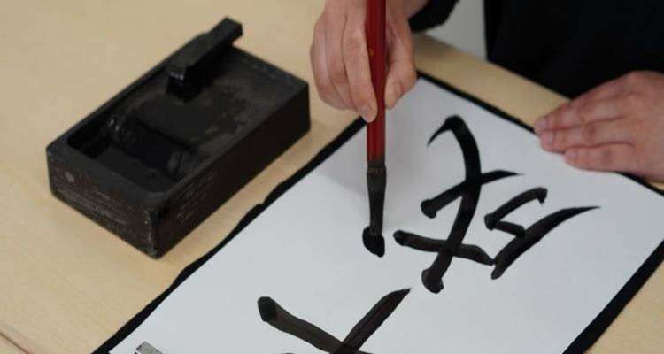 Primer plano de una persona practicando caligrafía japonesa con pincel y piedra de tinta