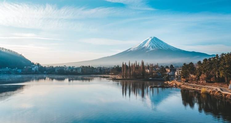 El Monte Fuji con las cimas nevadas reflejado en un lago tranquilo bajo un cielo azul y cristalino en la mañana