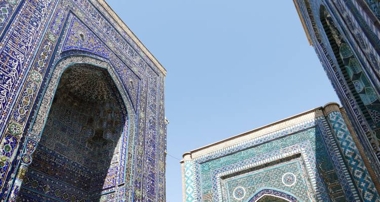 Perspectiva hacia arriba de muros y arcos de un mausoleo azul richamente azulejeado contra un cielo despejado