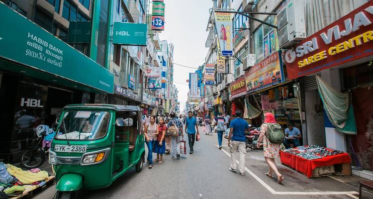 Drukke, smalle straatmarkt in Colombo met kleurrijke winkels en een groene tuk-tuk.