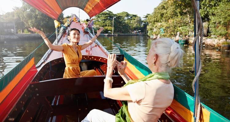 Deux femmes profitent d'une promenade en bateau à longue queue coloré le long d'un canal, l'une posant avec joie tandis que l'autre prend une photo.