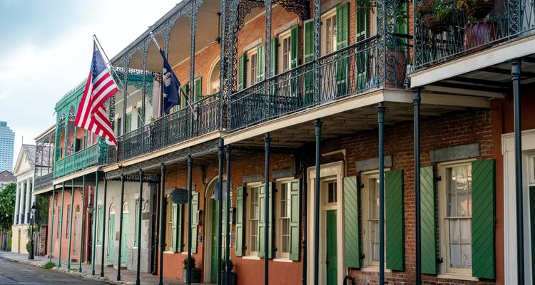 Des balcons en fer forgé historique ornés de drapeaux américains longeant une rue tranquille du Quartier français de la Nouvelle-Orléans.