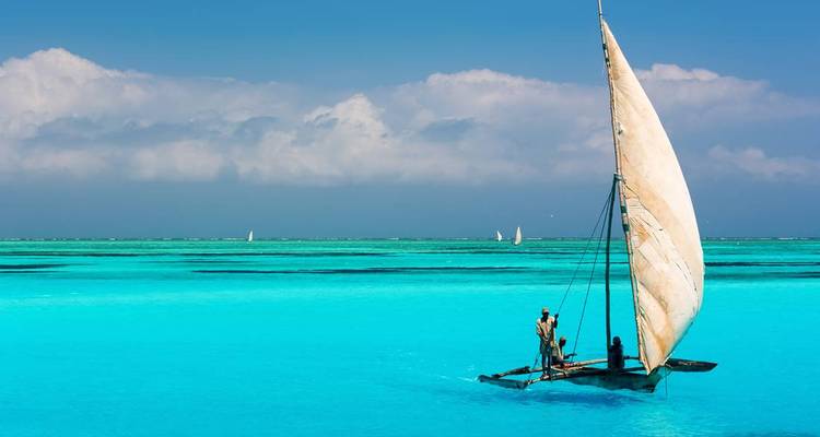 Un traditionnel voilier dhow glissant sur une eau turquoise cristalline sous un ciel bleu.