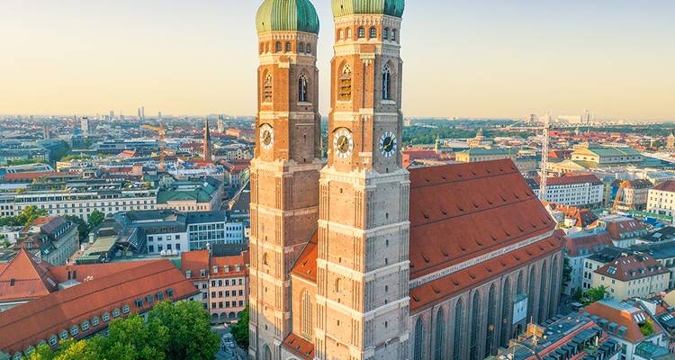 Vista aérea de las torres gemelas de la Frauenkirche de Múnich elevándose sobre los tejados rojos de la ciudad al amanecer.