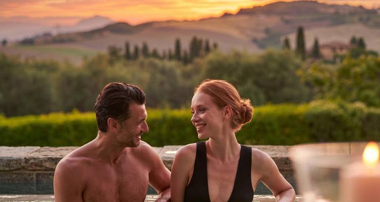 Gelukkig stel dat ontspant in een buitenopenluchtthermaal bad met rollende Toscaanse heuvels en een levendige zonsondergang op de achtergrond.