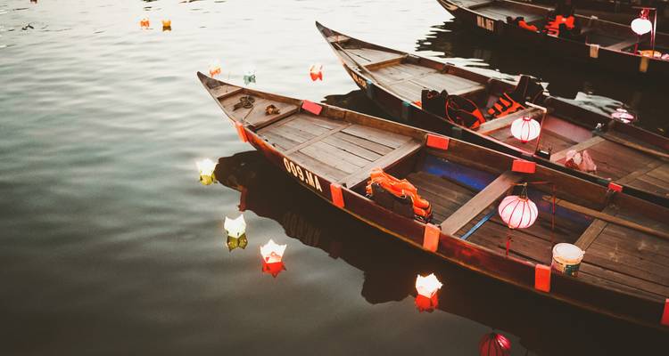 Les bateaux sampans en bois décorés de lanternes colorées flottent sur les eaux calmes de la rivière, créant des reflets.
