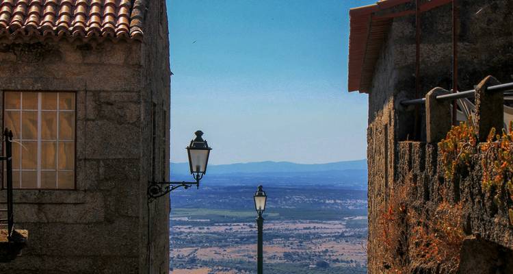 Callejón de piedra con farolas de hierro que enmarcan una vista del valle que se extiende lejos en la región de Castelo de Vide