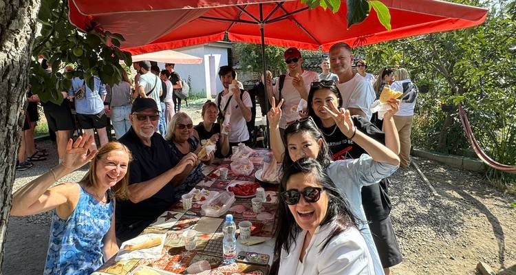Un groupe profitant d'un déjeuner pique-nique sous un parasol rouge, souriant et agitant la main vers l'appareil photo