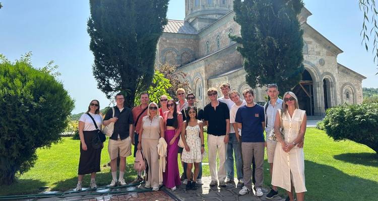 Groupe de touristes posant devant une cathédrale géorgienne et des cyprès par une journée ensoleillée