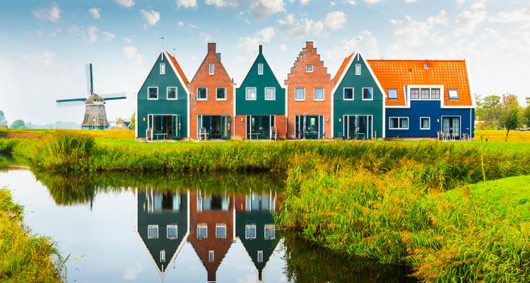 Fila de coloridas casas holandesas y un molino de viento reflejados perfectamente en un canal tranquilo.