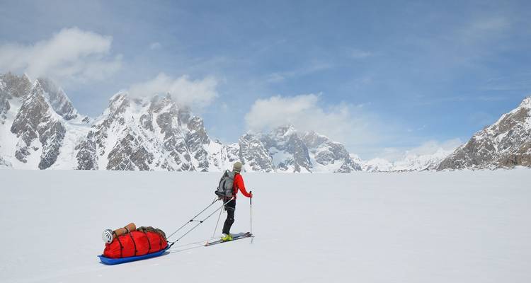 Solo skier hauling a sled across vast white glacier with jagged peaks in the distance.