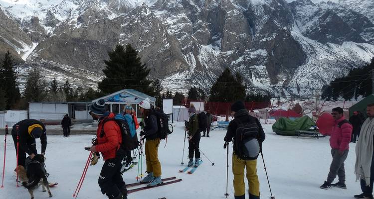 Skiers and guides prepare gear on snow field at mountain resort with tents and dogs.