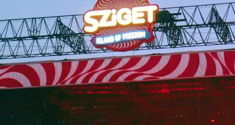 Señalización del escenario que dice 'Sziget - Island of Freedom' iluminada contra el cielo del atardecer.