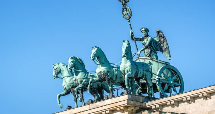 Primer plano de la estatua de cuadriga de bronce en la parte superior de la Puerta de Brandeburgo de Berlín recortada contra el cielo azul.