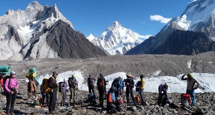 Trekking group resting on moraine with towering snow peaks behind in Pakistan.