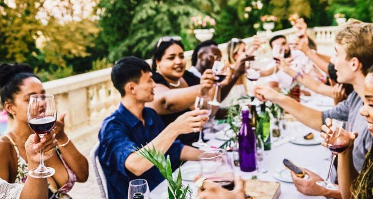 Long outdoor table of travellers raising glasses for a toast in a garden setting.