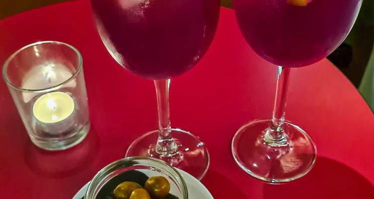 Close-up of two vibrant purple cocktails on a red table with candle and snack