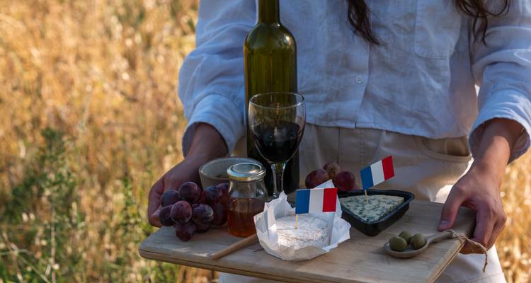 Outdoor platter with French cheese, honey, grapes and mini French flags held by person in linen shirt